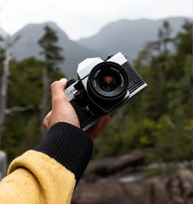 Une main masculine tenant un appareil photo devant un paysage rural